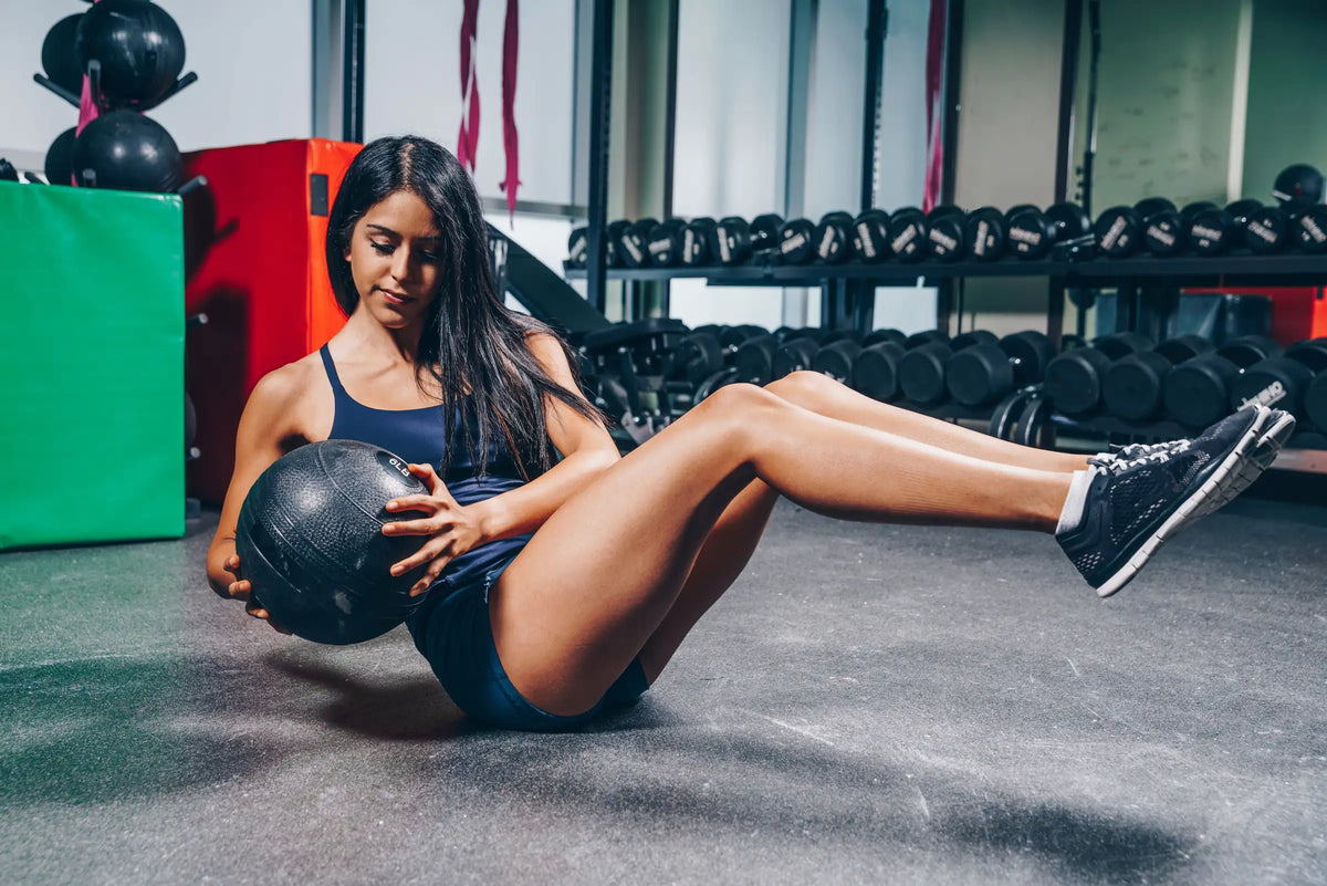 Woman performing a seated core exercise with a medicine ball in a gym